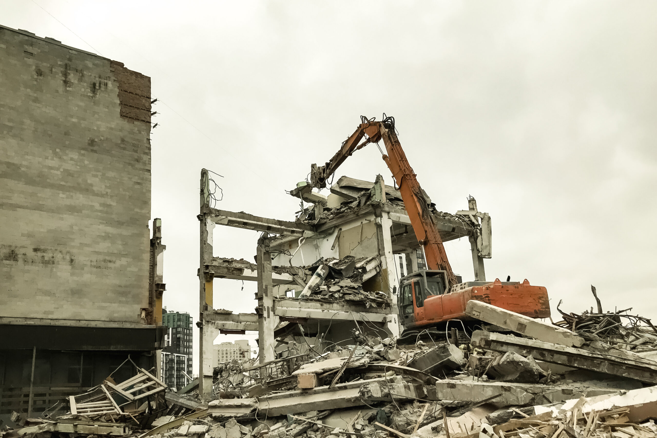 Hydraulic excavator demolition an old building at cloudy sky background. Heavy machinery taking down industry house on creation site for construction of new houses. Renovation concept. Copy text space